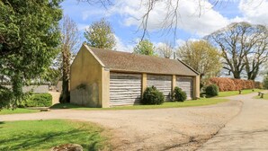 A rustic wooden building with a sloped roof, surrounded by a gravel driveway and a well-maintained lawn. - Swallow Studio (Cheltenham)