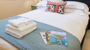 A neatly made bed with a blue and white patterned bedspread, a stack of white towels, a decorative pillow with a red and blue design, and a magazine titled 'COUNTRY LIFE' on the bed. - Swallow Studio (Cheltenham)