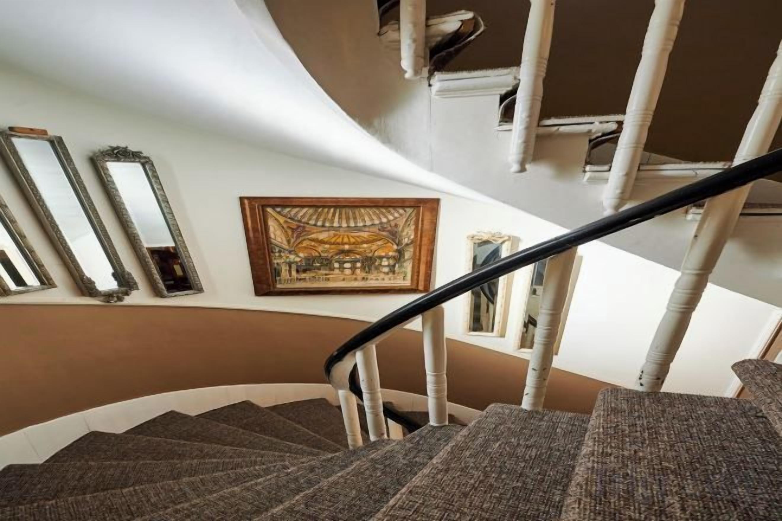 A spiral staircase with a handrail, a framed picture on the wall, and a window to the right.