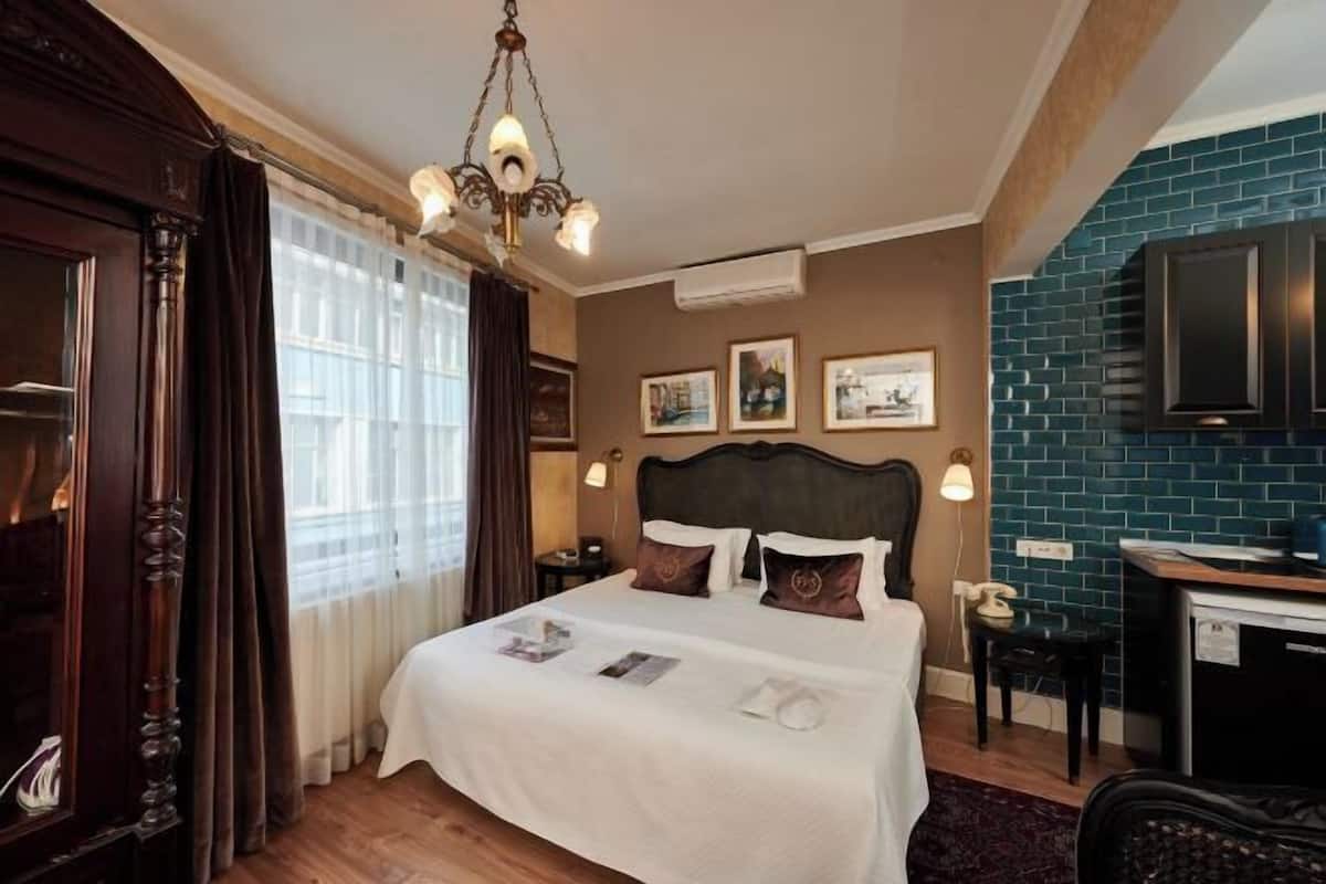 A hotel room with a large bed, a desk, a chair, a chandelier, and a blue-tiled wall.