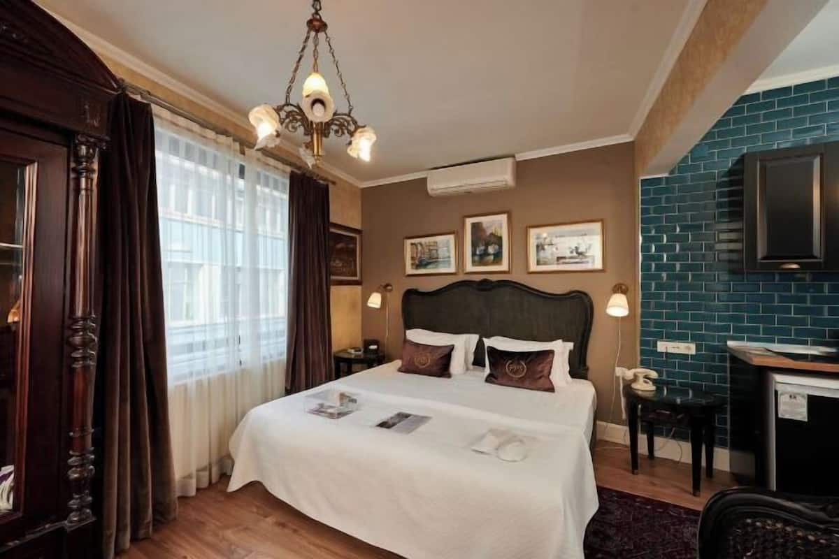 A hotel room with a bed, a desk, a chair, a chandelier, and artwork on the wall.