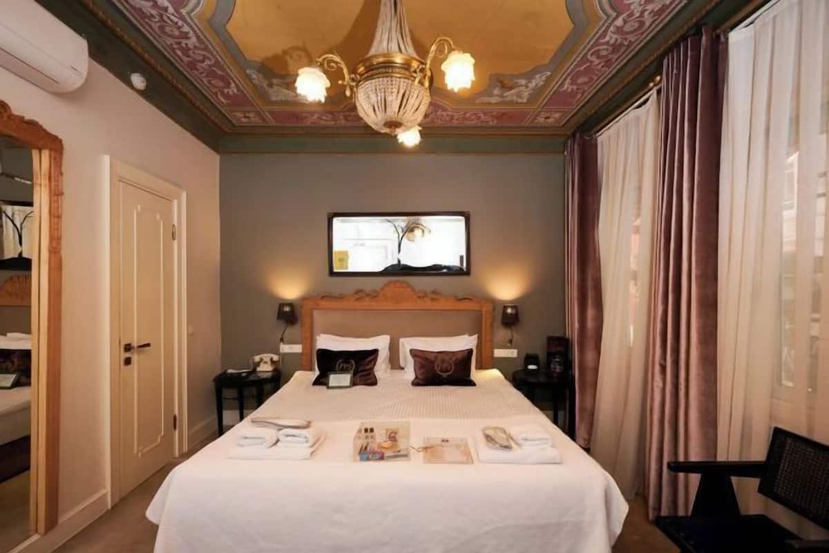 A hotel room with a large bed, a chandelier, a television, and a desk with a telephone.