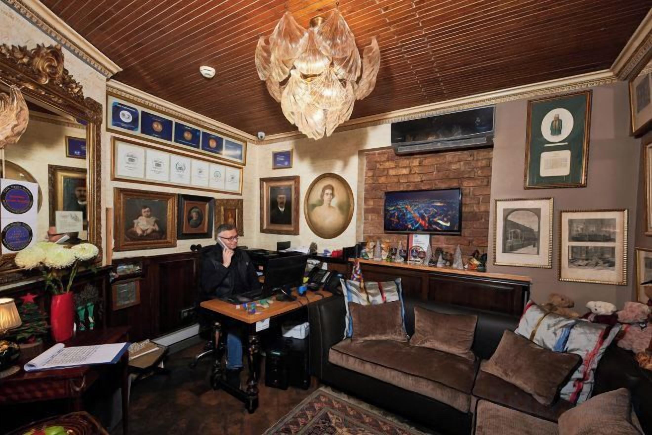A room with a wooden ceiling, a chandelier, a fireplace, and various framed pictures and certificates on the walls.