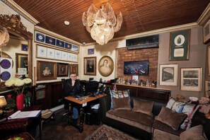 Une pièce avec un plafond en bois, un lustre, une cheminée, ainsi que divers tableaux et certificats encadrés accrochés aux murs.