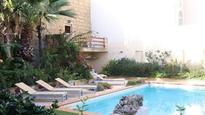 Un espace piscine agrémenté de chaises longues, d’un élément décoratif en roche et d’une végétation luxuriante.