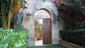 Un arc en pierre menant à une porte en bois, entouré d’une végétation luxuriante et de plantes en pot.