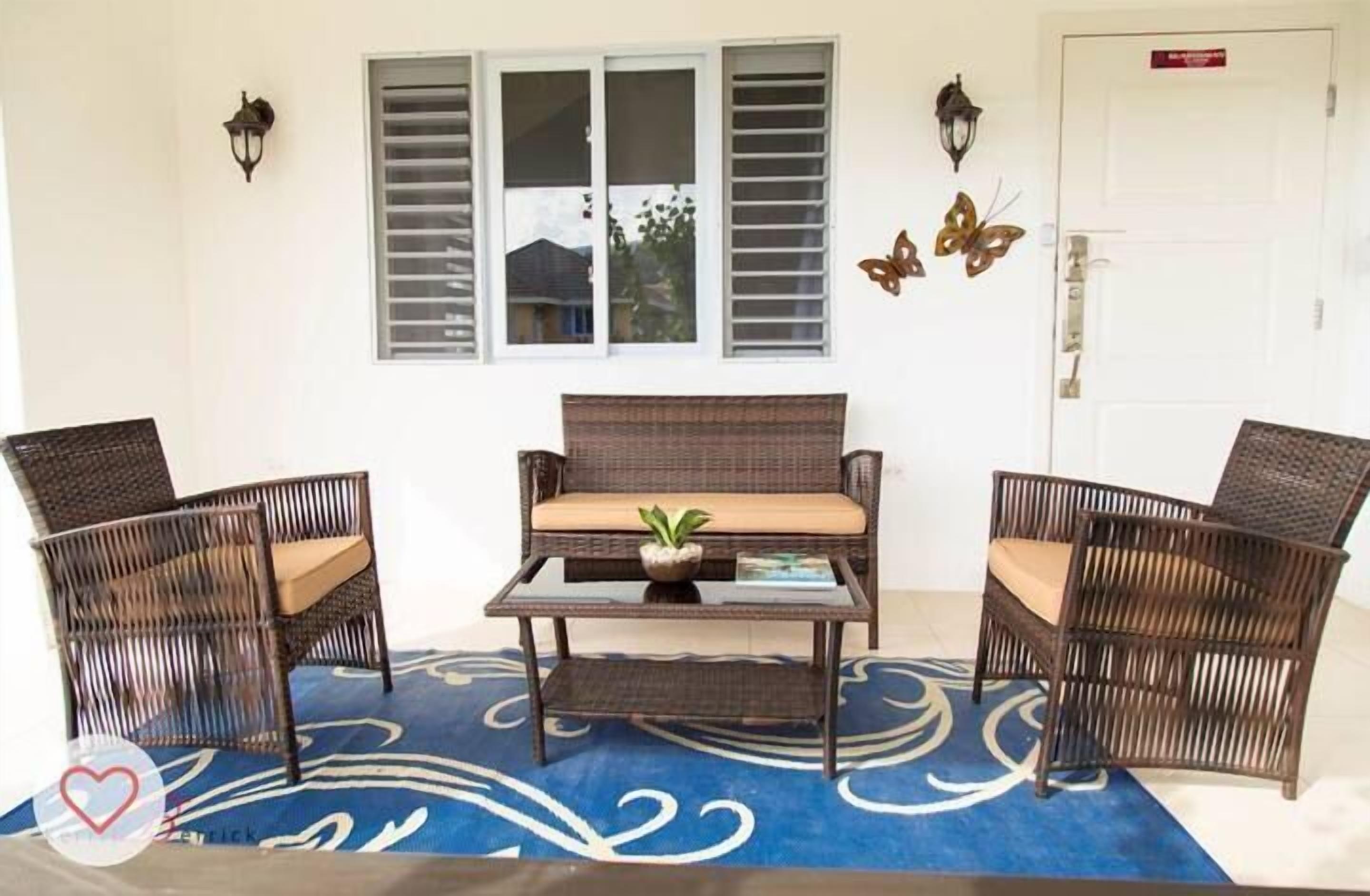 A room with a wicker sofa set, two chairs, a small table, and a potted plant.