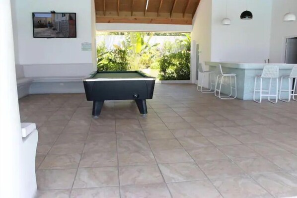 A pool table in a room with a tiled floor, a bar area with white bar stools, and a view of greenery outside. - Relaxing Stay - Richmond Estate - 15mins Ocho Rios (St. Ann's Bay)