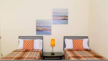 Habitación de hotel con dos camas, cada una con colcha a cuadros y almohadas estampadas. Hay dos cuadros colgados en la pared que representan paisajes.