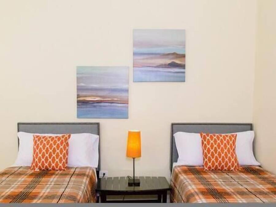 Habitación de hotel con dos camas, cada una con colcha a cuadros y almohadas estampadas. Hay dos cuadros colgados en la pared que representan paisajes.