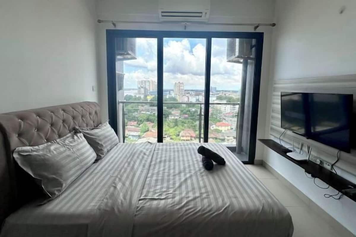 Ein Schlafzimmer mit einem großen Bett, einem Fernseher und Blick auf die Stadt durch ein großes Fenster.
