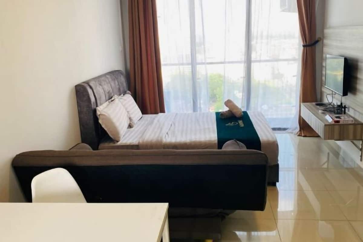 Ein Hotelzimmer mit Bett, Sofa, Fernseher und einem Fenster mit Vorhängen.
