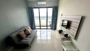 A modern living room with a grey sofa, a flat-screen TV mounted on a wooden panel, and a sliding glass door leading to a balcony. - Sky River Front Kota Bharu @ AGhome (Kota Bharu)