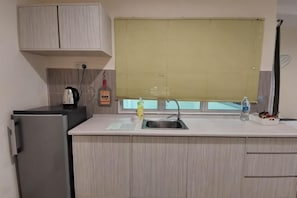 A kitchen with a refrigerator, sink, window with blinds, and a kettle. - Rustic One Bedroom Unit for 4Pax by Jomy Management (Manjung)