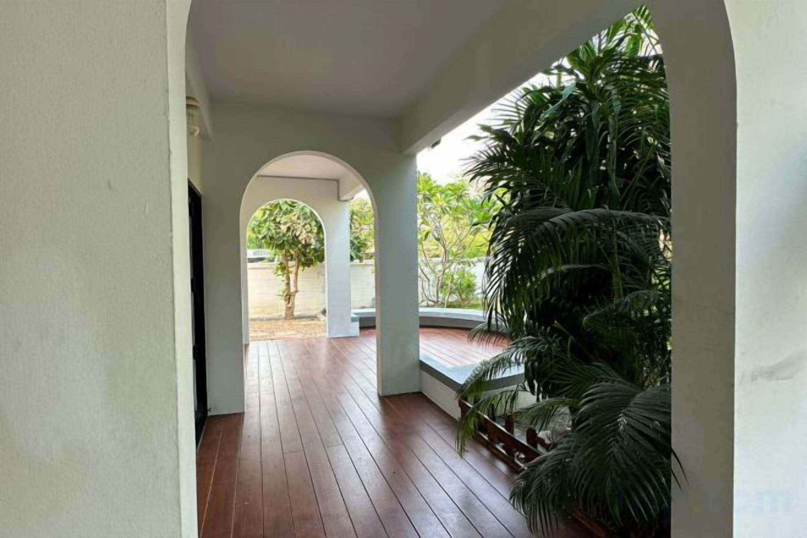 A covered outdoor area with a wooden floor, an arched doorway, and potted plants.