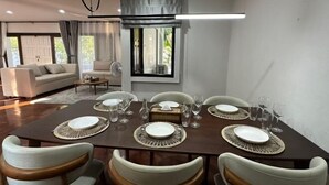 A dining area with a dark wooden table set for six, surrounded by white upholstered chairs. - Bangkok Cozy Garden Pool Villa Sukhumvit (Bangkok)
