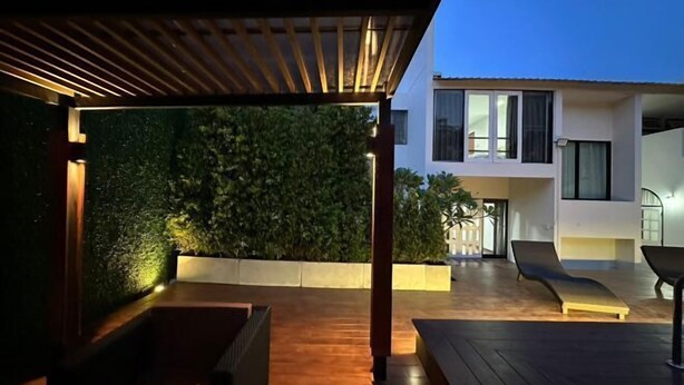 An outdoor patio area with a wooden deck, a seating area, and a modern building in the background. - Bangkok Cozy Garden Pool Villa Sukhumvit (Bangkok)