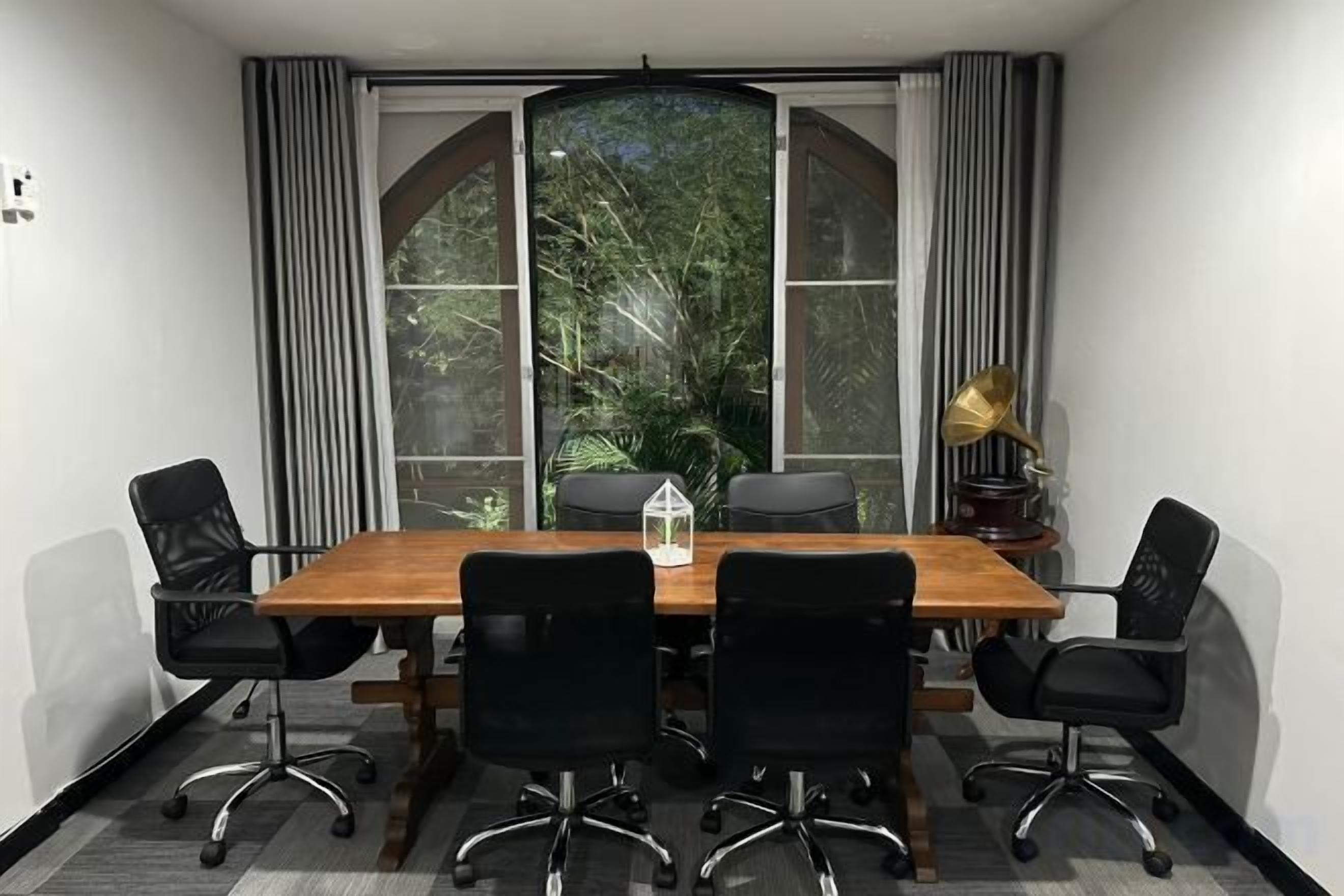 A conference room with a wooden table, six black chairs, and a large window with curtains.