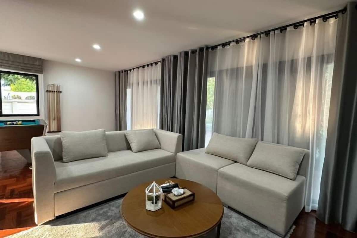 A modern living room with two sofas, a coffee table, and a view through sheer curtains.
