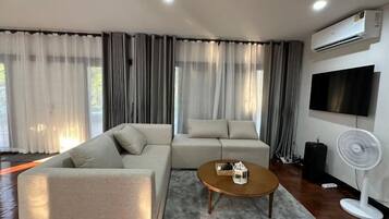 Un salon moderne avec un canapé d’angle, une table basse et un téléviseur à écran plat fixé au mur.