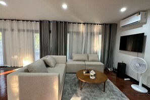 A modern living room with a sectional sofa, a coffee table, and a flat-screen TV mounted on the wall.