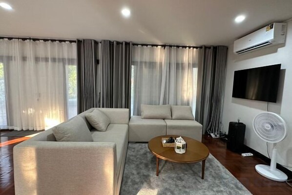 A modern living room with a sectional sofa, a coffee table, and a flat-screen TV mounted on the wall.