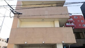 A multi-story building with a flat facade, balconies, and a ground-level entrance with a door and a sign. - Tasone Stay OSAKA SL610 (Osaka)