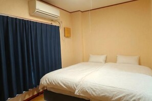 Et hotelværelse med en seng, gardiner, en klimaanlæg og en vægmonteret lampe.