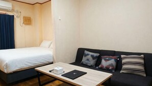 A room with a bed, a sofa, a table with a laptop, and a wall-mounted air conditioner. - Tasone Stay OSAKA SL610 (Osaka)