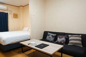 Et værelse med en seng, en sofa, et bord med en bærbar computer og en vægmonteret aircondition.