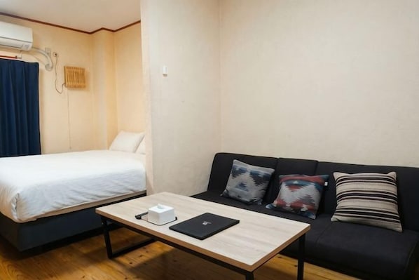 Une pièce comprenant un lit, un canapé, une table avec un ordinateur portable et un climatiseur fixé au mur.
