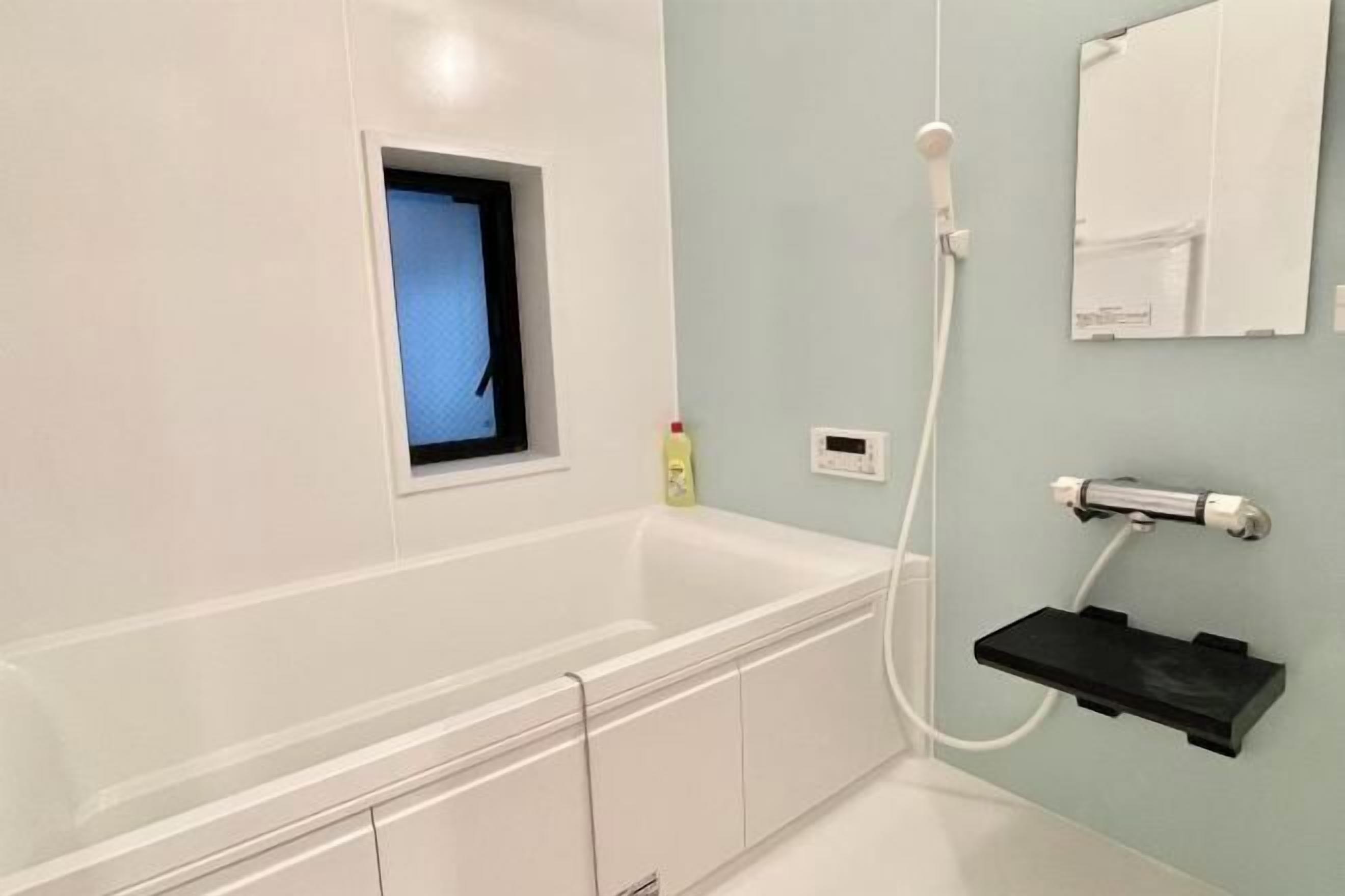 A bathroom with a white bathtub, a small window, a handheld showerhead, and a wall-mounted sink.