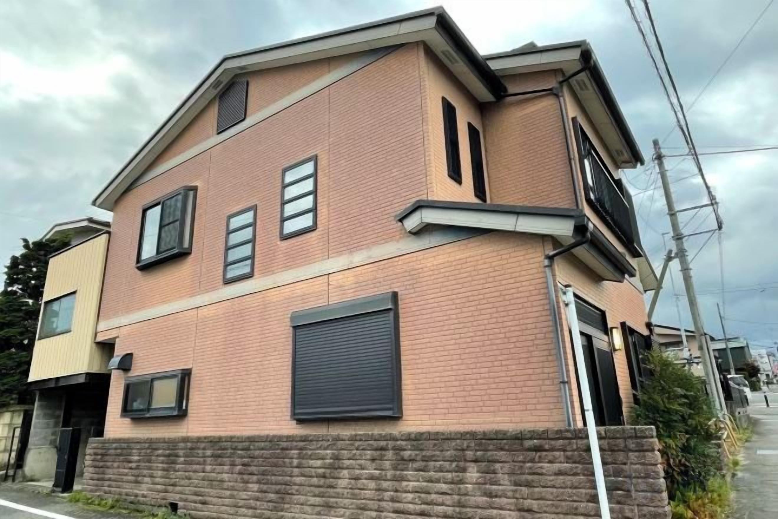 Un edificio residenziale a due piani con facciata in mattoni, un portone per garage e un vialetto visibile.