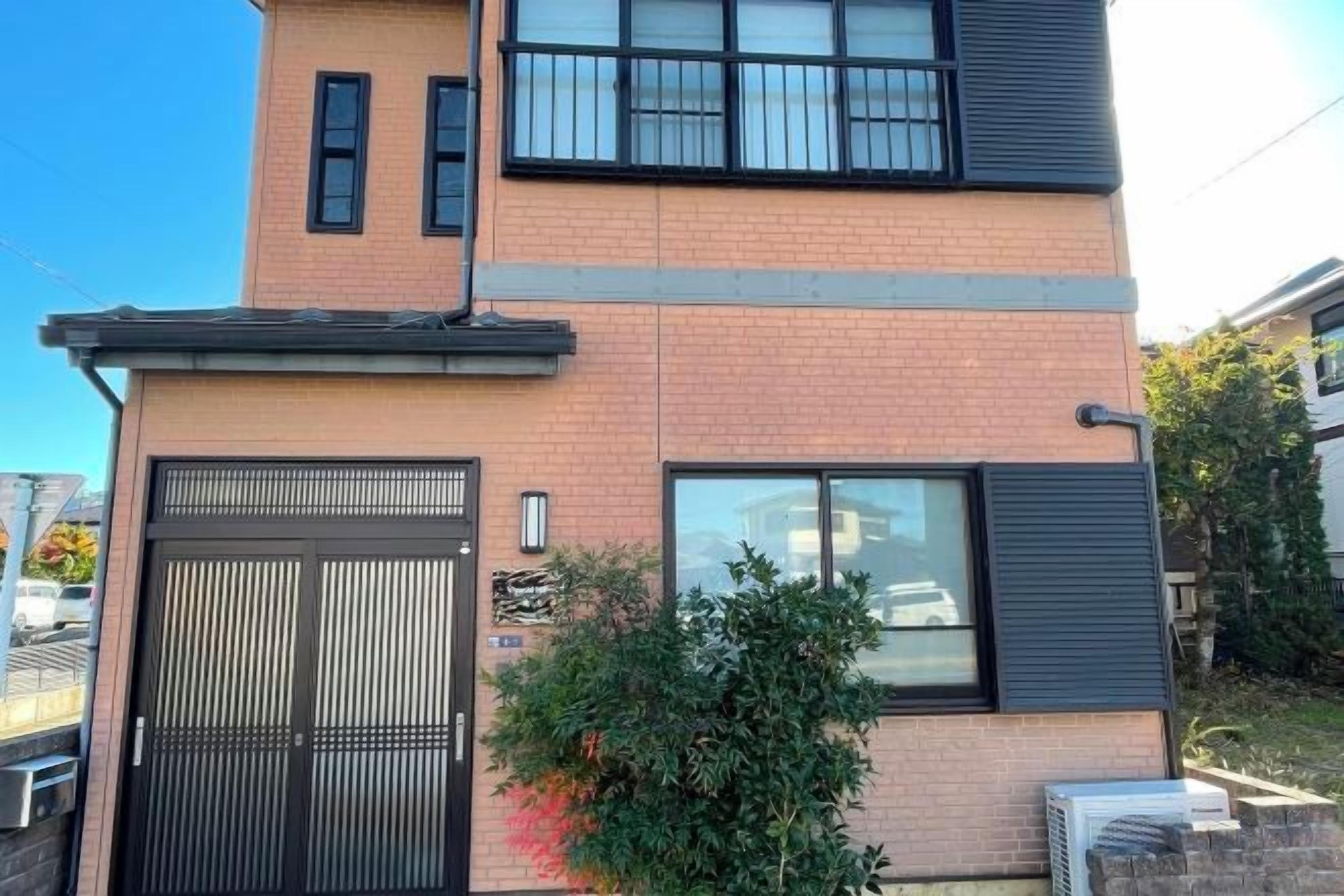 A two-story building with a black door, a window with black shutters, and a small green bush in front.