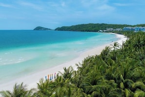 A beach with clear turquoise water, a sandy shore, and a line of palm trees. - SEA GALLERY TROPICAL VILLAS KHEM BEACH (Phu Quoc Island)