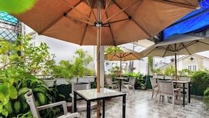 An outdoor patio area with tables and chairs, surrounded by potted plants and umbrellas.