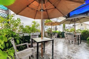 Eine Terrassengruppe mit Tischen und Stühlen, beschattet durch Sonnenschirme, umgeben von Grünpflanzen.