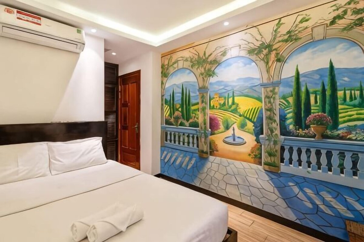 A hotel room with a bed, a mural, a balcony, and an air conditioning unit.