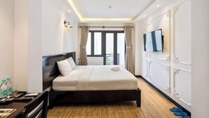 A hotel room with a bed, a TV, a desk with a chair, and a window with curtains.
