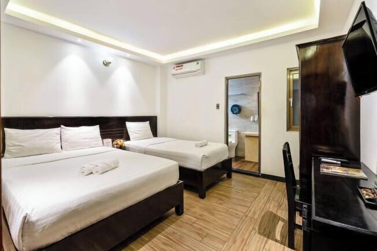 Habitación de hotel con dos camas, un televisor de pantalla plana, piso de madera y una puerta que da a un baño.