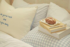 A neatly made bed with a pillow featuring text, a stack of books, and a plate with a pastry. - Hongik Univ. Station Romantic Rooftop House (Seoul)