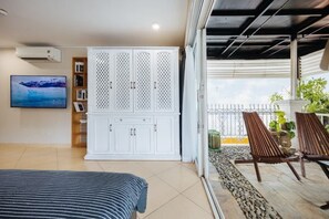 A bedroom with a bed, a white wardrobe, a TV, and a balcony with chairs and plants. - VietHOME - 22 Pho Hue - Apartment 702 (Hanoi)