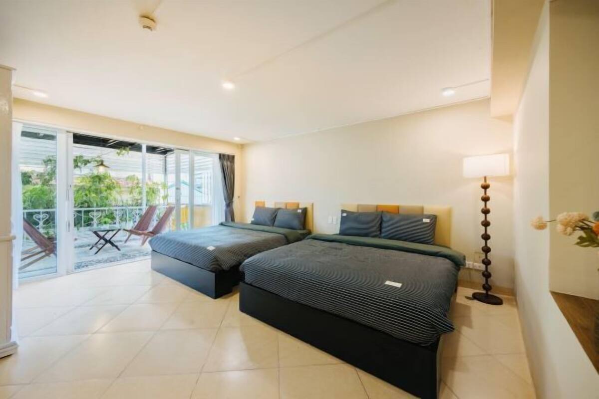 A hotel room with two beds, a balcony with chairs, and a lamp.