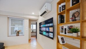 A hallway with a digital display, a bookshelf with magazines, and a window with flowers. - VietHOME - 22 Pho Hue - Apartment 702 (Hanoi)