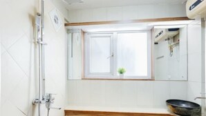 A bathroom with a shower, a sink with a large basin, and a window above the mirror. - VietHOME - 22 Pho Hue - Apartment 702 (Hanoi)