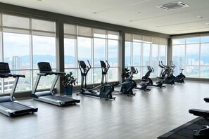 Une salle de sport équipée de matériel d’exercice et dotée de grandes fenêtres donnant sur un panorama urbain.