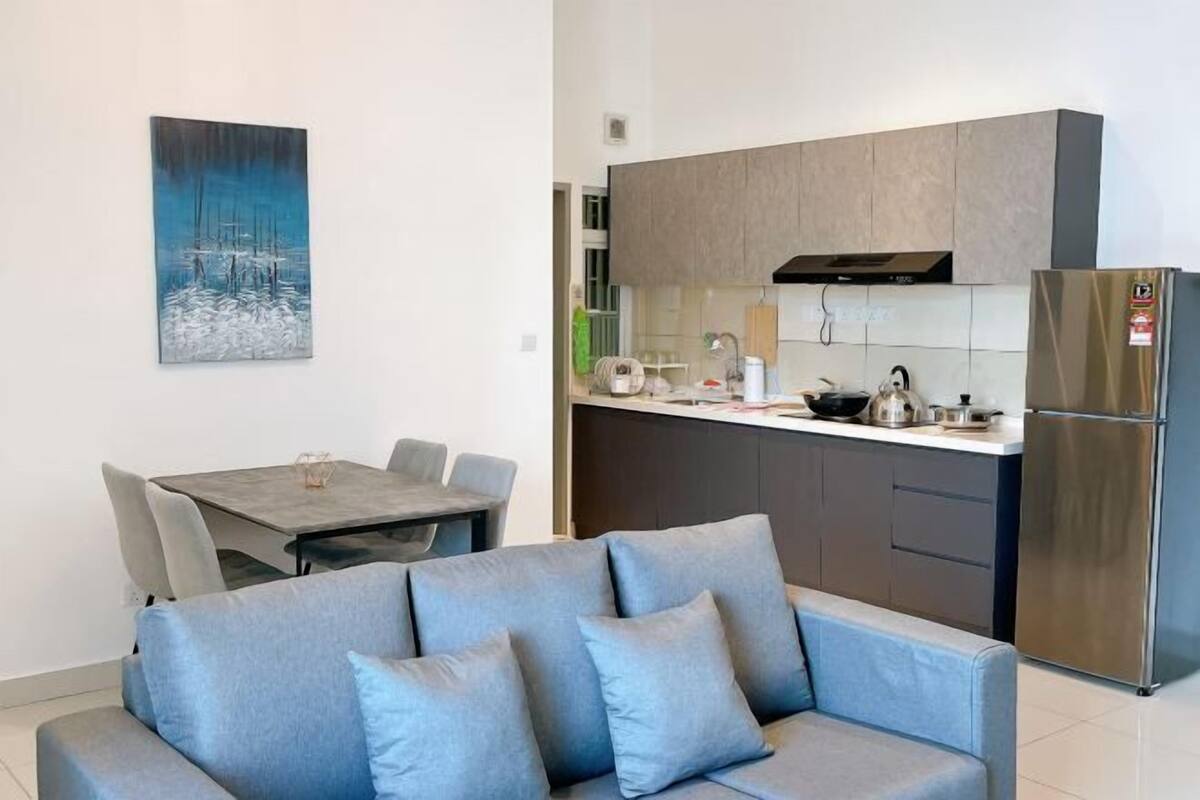 Eine moderne Küche mit grauen Schränken, einem Edelstahlkühlschrank und einem Essbereich mit grauem Sofa und Tisch.
