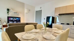 A modern living room with a dining table set for six, a sofa, a flat-screen TV, and a kitchen area with cabinets and a refrigerator. - TR Residence Titiwangsa By Iconique (Kuala Lumpur)