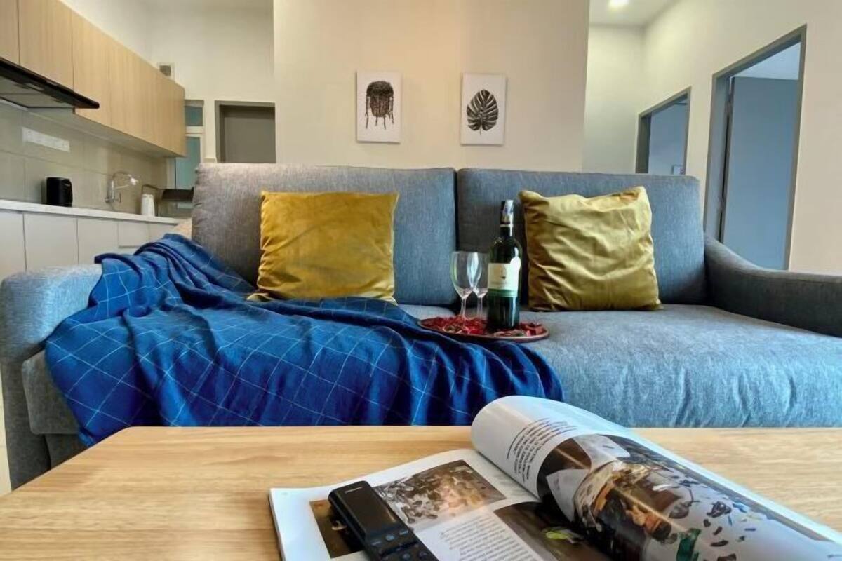 Ein modernes Wohnzimmer mit einer Couch, Kissen, einer Zeitschrift, einer Fernbedienung und einem Glas Wein auf einem Tablett.