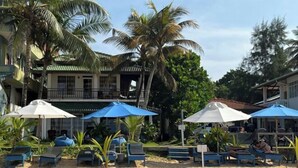 Un resort frente al mar con sillones de playa y sombrillas, palmeras y un edificio con balcón.